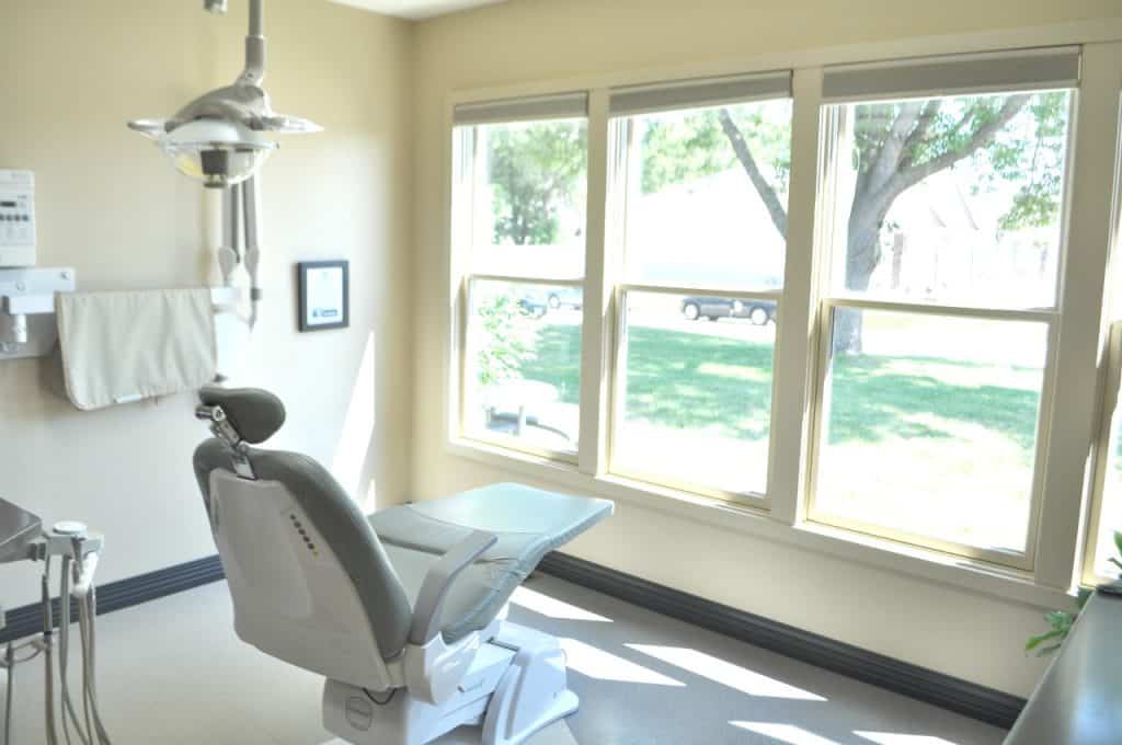 A dental exam room with a dental chair in the middle facing a row of windows