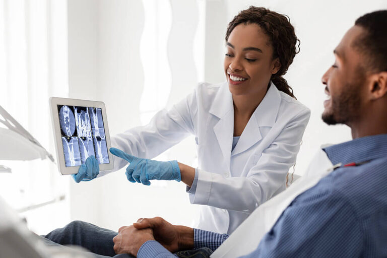 A female dentist holds a dental x-ray while explaining root canal steps to a patient