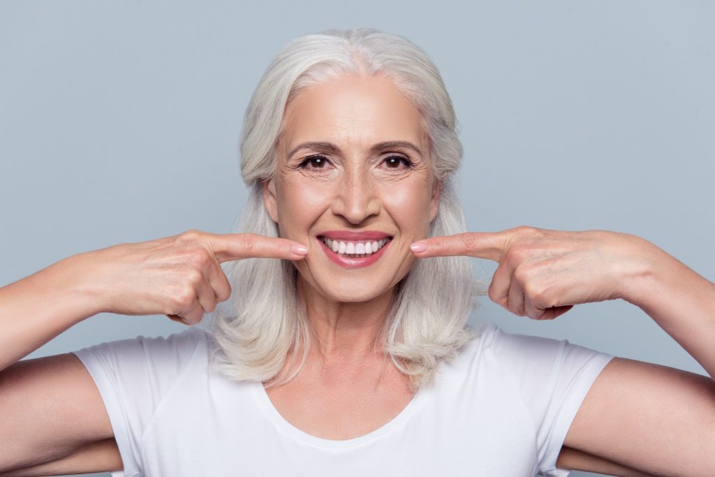 An older woman smiling and pointing to her bright, white teeth