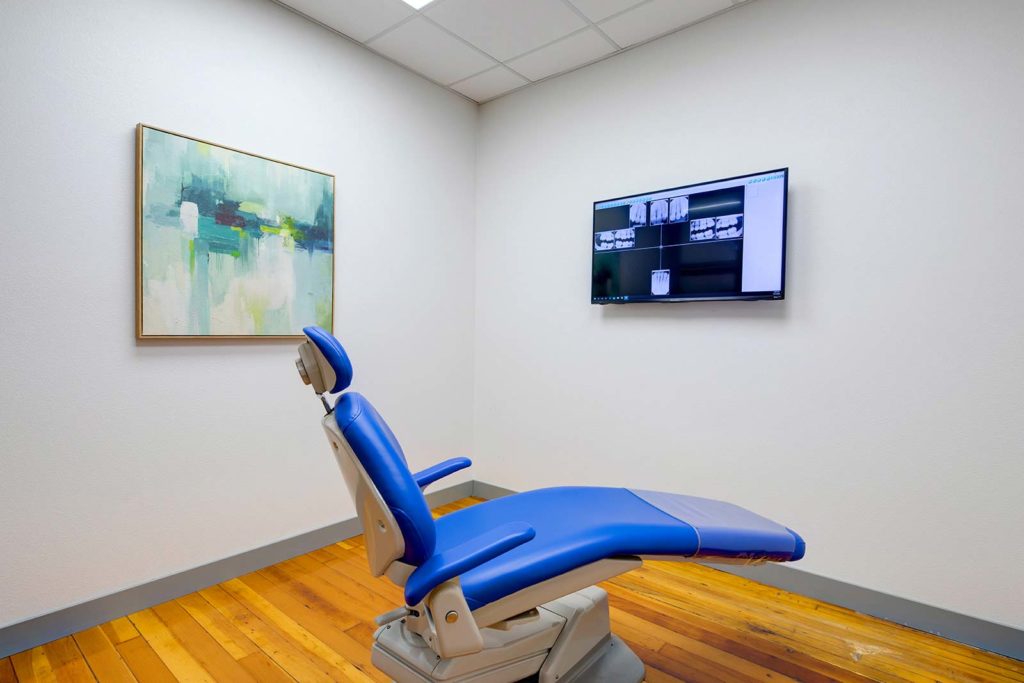 A patient room at one of The Dentist of Siouxland offices with a dental chair in the middle facing a tv on the wall