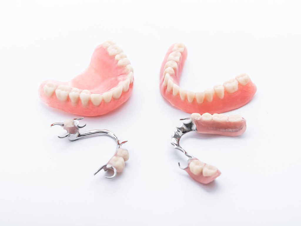A set of full dentures and a set of partial dentures laying on a white background