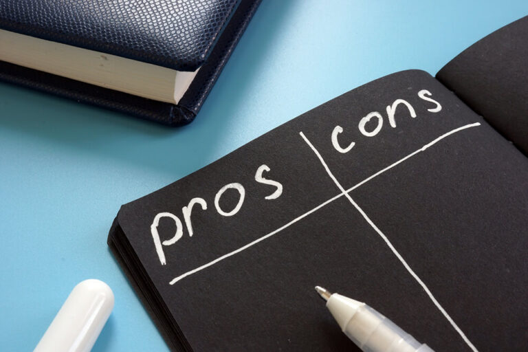 Notebook open to a 'pros and cons' list with white ink, and a white pen resting on the notebook.